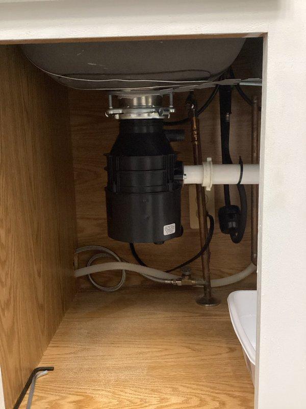 # Garbage Disposal Installation

Completed installation of new garbage disposal unit under kitchen sink. Removed existing disposal and connected replacement unit to sink drain with proper mounting flange assembly. Established electrical connection to dedicated outlet within cabinet. Connected white PVC discharge piping from disposal to existing drain line and secured dishwasher drain connection to disposal inlet. Verified all plumbing connections for proper seal and tested disposal operation under running water to confirm proper function and drainage. Placed leak detection tray beneath disposal unit as precautionary measure. System operating properly with no leaks detected.