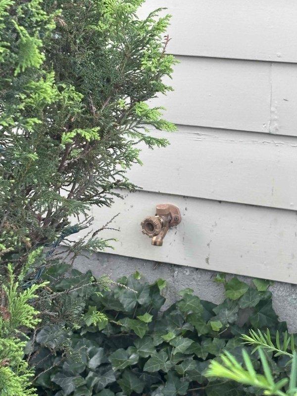 Completed replacement of exterior hose bib on building with horizontal siding. Removed aged copper-colored fixture showing oxidation and installed new hose bib, restoring proper function to outdoor water supply connection.