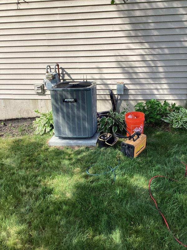 Successfully completed full air conditioning system replacement at residential property. Removed existing outdoor condensing unit and installed new blue-gray condenser on concrete pad against exterior wall with proper clearances maintained. Unit positioned on stable concrete foundation with adequate airflow access on all sides. Utilized refrigerant recovery equipment to properly evacuate and reclaim refrigerant from old system in compliance with EPA regulations. Established refrigerant line connections using manifold gauges and charging hoses, ensuring proper vacuum and leak testing procedures. Connected new condensing unit to existing indoor air handler system located in basement utility area. Verified all electrical connections, ductwork integration, and condensate drainage systems functioning properly. Performed system startup, checked refrigerant charge levels, and confirmed optimal operating pressures and temperatures. All work completed to manufacturer specifications and local co