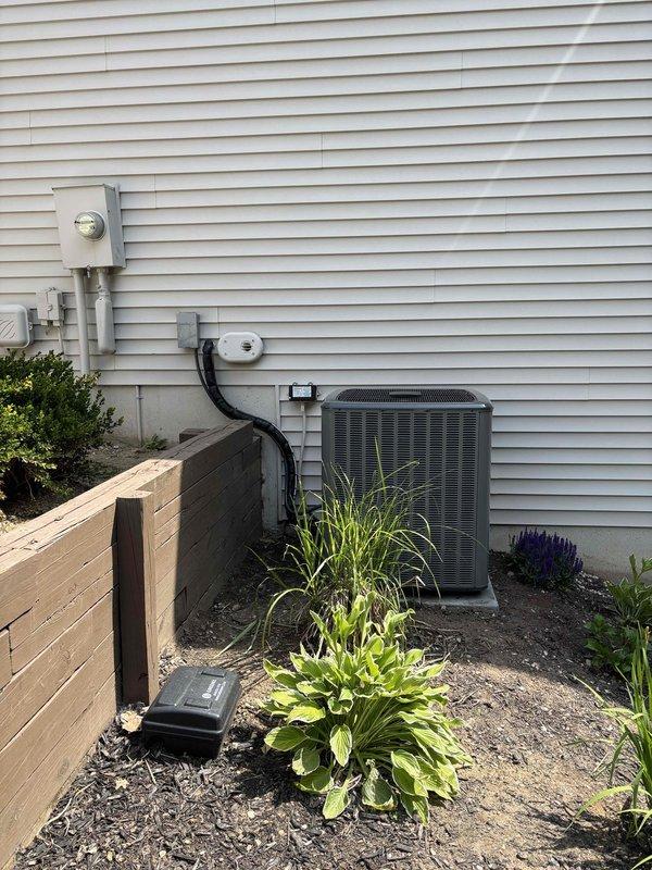 Successfully completed full air conditioning system replacement at residential property. Removed existing outdoor condensing unit and installed new HVAC condensing unit on exterior wall adjacent to existing electrical meter. Secured refrigerant lines along vinyl siding using proper mounting brackets and ensured all copper refrigerant piping connections were properly fitted with brass fittings and insulated with foam sleeves where required. Verified factory charge specifications, completed all electrical connections, and confirmed system operational parameters meet manufacturer specifications. Unit positioned in existing location within landscaped area to maintain aesthetic integration with property.