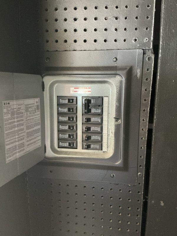 Completed electrical estimate for insurance claim on manufactured home with downed wire at rear of property. Assessed damaged electrical panel and compromised underground wiring requiring full replacement. Documented existing Eaton breaker panel, exterior meter housing, and conduit system with photographic evidence showing weathered components and structural damage at roof line near service entrance for claim submission.