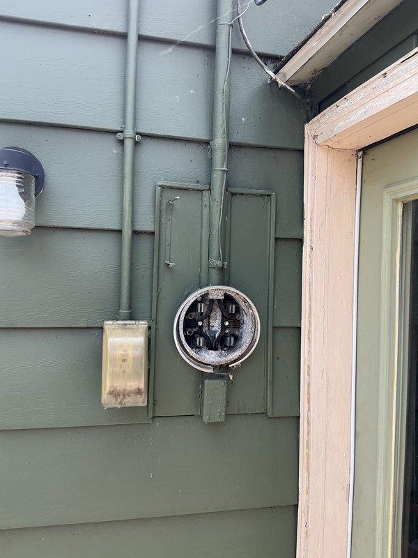 Completed electrical estimate for insurance claim on manufactured home with downed wire at rear of property. Assessed damaged electrical panel and compromised underground wiring requiring full replacement. Documented existing Eaton breaker panel, exterior meter housing, and conduit system with photographic evidence showing weathered components and structural damage at roof line near service entrance for claim submission.
