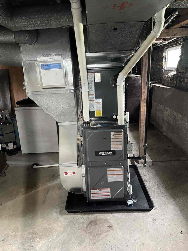 Complete residential HVAC system installation performed, including new furnace and air conditioning condenser unit. Furnace installed in basement utility area on raised platform with proper clearances, connected to new metallic supply ductwork and PVC condensate drainage system. Air handler positioned adjacent to furnace with digital control panel for system management. Outdoor AC condenser unit installed on concrete pad with proper leveling, positioned on house exterior with adequate clearance from structure. Refrigerant lines run from condenser through foundation to indoor equipment with appropriate insulation. Electrical disconnect box mounted on dedicated pole near outdoor unit for service accessibility. All connections made to existing electrical service panel and meter. System commissioned and verified for proper operation of both heating and cooling functions.