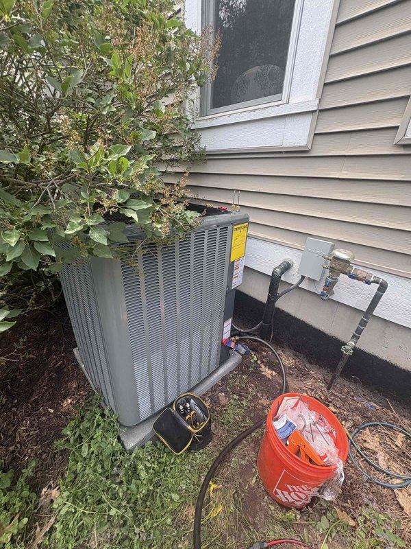 Successfully completed full HVAC system replacement including outdoor condenser unit and indoor furnace. Removed existing equipment and installed new gray condenser unit on exterior with proper refrigerant line connections, copper piping, and black insulation. Configured all plumbing connections and secured unit against exterior wall with appropriate clearances. Indoor installation included new furnace unit in basement utility area with associated PVC venting system routed vertically for proper exhaust. Connected all electrical components, refrigerant lines, and ductwork to complete system integration. Verified all connections, tested system operation, and confirmed proper airflow throughout. Work area cleaned and all debris removed upon completion.