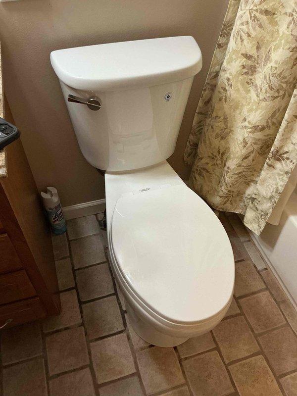 Responded to service call for leaking toilet requiring replacement. Upon arrival, assessed existing two-piece white porcelain toilet with chrome flush lever and dual-flush mechanism showing signs of water leakage at base. Documented pre-existing conditions through photographic documentation. Evaluated bathroom layout including tile flooring and surrounding fixtures to determine proper replacement specifications and installation requirements.