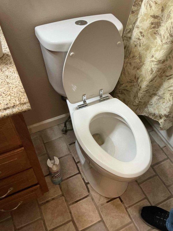 Responded to service call for leaking toilet requiring replacement. Upon arrival, assessed existing two-piece white porcelain toilet with chrome flush lever and dual-flush mechanism showing signs of water leakage at base. Documented pre-existing conditions through photographic documentation. Evaluated bathroom layout including tile flooring and surrounding fixtures to determine proper replacement specifications and installation requirements.
