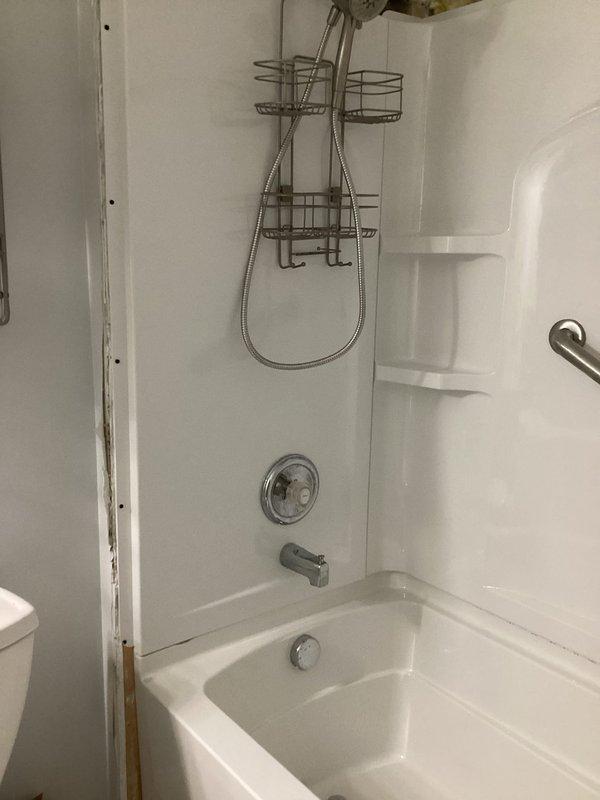 # PRMISC-Misc Plumbing Repair

## Work Performed

Responded to service call for tub and shower unit requiring assessment and repair. Upon arrival, conducted thorough inspection of white fiberglass bathtub and shower surround combination unit. 

Identified significant water damage along right edge of shower surround where wall panel meets adjacent wall surface. Noted exposed brown wooden framing material with visible water intrusion damage, including yellowish-green staining at base near tub edge, indicating prolonged moisture exposure. Deterioration pattern suggested compromised seal between surround panel and wall structure, allowing water to penetrate behind shower enclosure.

Documented existing bathroom fixtures including chrome shower head with flexible metal hose, circular temperature control valve, tub spout, and properly functioning drain. Verified two brushed nickel grab bars mounted on shower walls for safety compliance. Observed hanging chrome shower caddy organizer suspende