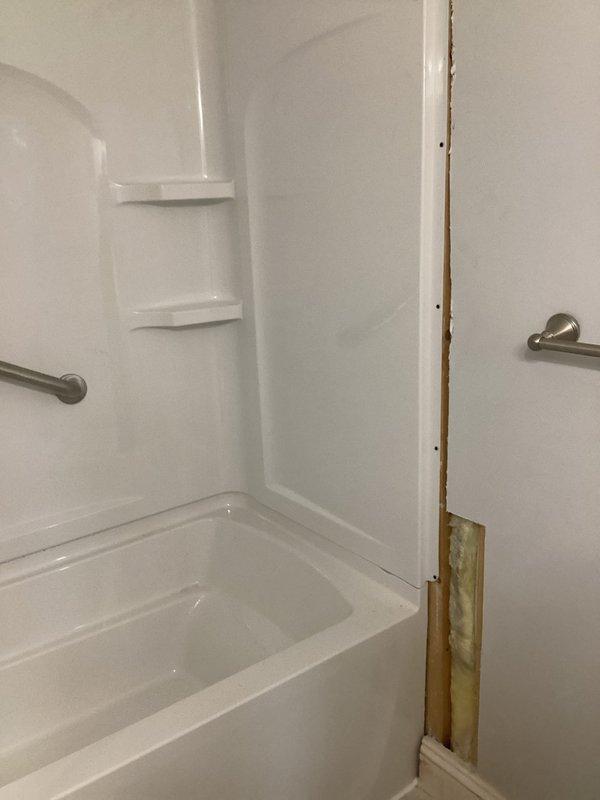 # PRMISC-Misc Plumbing Repair

## Work Performed

Responded to service call for tub and shower unit requiring assessment and repair. Upon arrival, conducted thorough inspection of white fiberglass bathtub and shower surround combination unit. 

Identified significant water damage along right edge of shower surround where wall panel meets adjacent wall surface. Noted exposed brown wooden framing material with visible water intrusion damage, including yellowish-green staining at base near tub edge, indicating prolonged moisture exposure. Deterioration pattern suggested compromised seal between surround panel and wall structure, allowing water to penetrate behind shower enclosure.

Documented existing bathroom fixtures including chrome shower head with flexible metal hose, circular temperature control valve, tub spout, and properly functioning drain. Verified two brushed nickel grab bars mounted on shower walls for safety compliance. Observed hanging chrome shower caddy organizer suspende