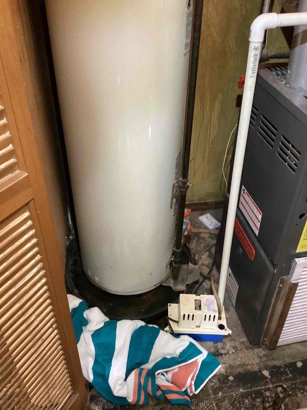 Provided estimate for replacement of 33-year-old water heater that has exceeded twice its expected lifespan and is actively leaking, causing water damage to surrounding area. Assessment included evaluation of current placement and potential relocation of unit due to space constraints and accessibility concerns. Documented existing conditions showing aged galvanized piping, deteriorated wooden framing with moisture damage, and compromised floor area requiring remediation during installation.