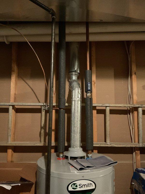 Responded to service call regarding slow-flushing toilet and banging noise in plumbing when washing machine operates. Inspected water heater installation and associated piping system in utility area. Observed condensation on vertical discharge piping from water heater, indicating potential thermal expansion issues that may contribute to hydraulic shock (water hammer) during appliance operation. Evaluated plumbing configuration and drainage system accessibility through wall access panel near laundry area. Documented conditions of water supply lines, discharge piping, and connections to identify source of pressure fluctuations causing banging noise and restricted toilet flush performance.