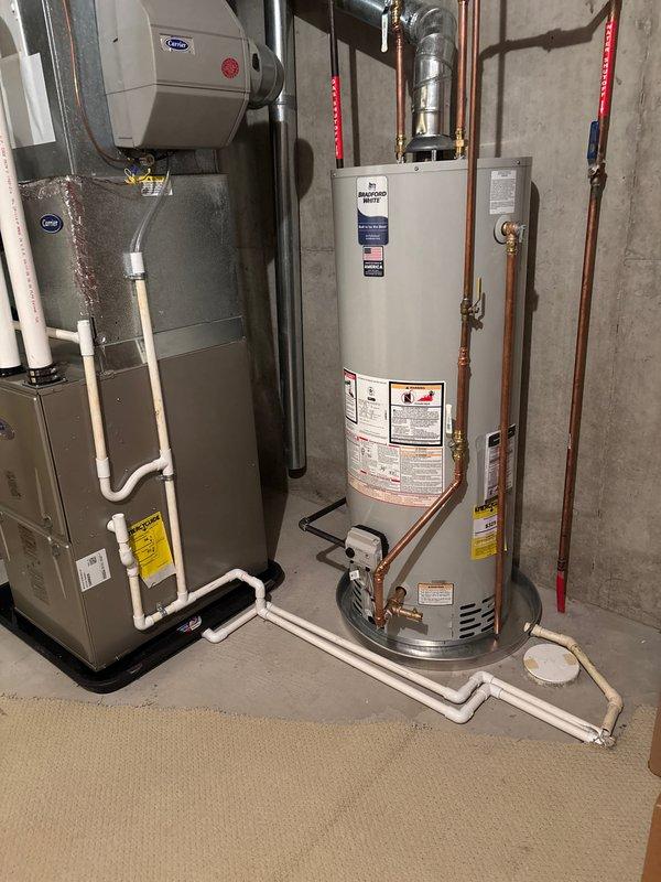 Successfully completed full installation of new Carrier furnace and Bradford White water heater in basement mechanical room. Installed gray metal furnace unit with proper PVC condensate drainage lines routed along floor. Mounted new cylindrical water heater with copper supply piping, red-handled shut-off valves, and silver expansion tank connected to top of unit. Integrated barrel-style humidifier system to furnace with appropriate ductwork connections. All metal ductwork properly connected and secured. Verified all gas connections, electrical hookups, and venting systems meet code requirements. System tested and operational.