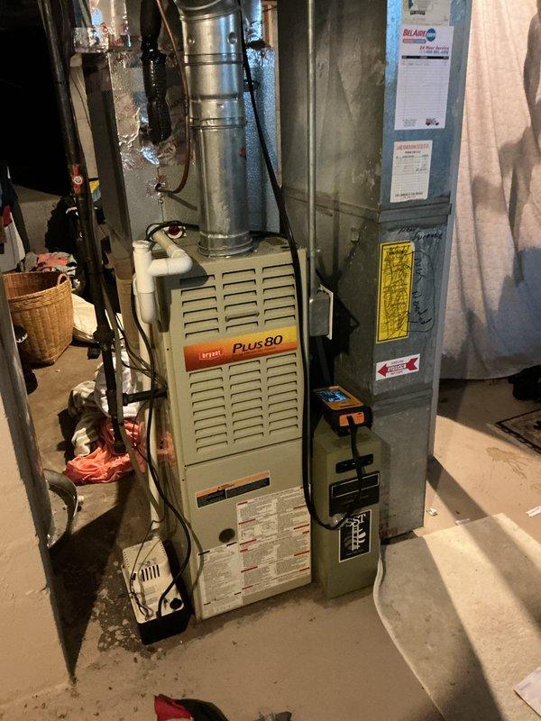 Completed rental inspection of 24-year-old Bryant Plus 80 furnace system. Documented equipment condition through photographs, noting deteriorated wall penetration around flexible ductwork with cracked and crumbling plaster surrounding the duct connection point requiring attention. Verified furnace model information and assessed overall HVAC system condition in basement mechanical room.