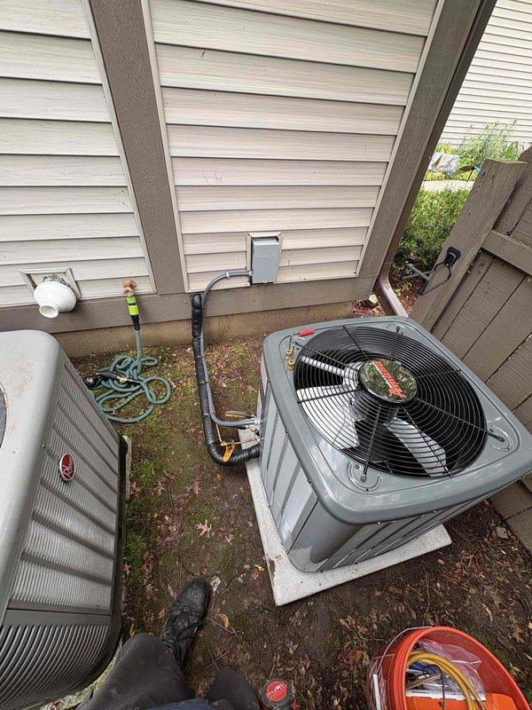 Completed full installation of residential HVAC system including new furnace and air conditioning condenser unit. Installed gray furnace unit in basement mechanical room with proper venting through white PVC piping and connected metallic ductwork with reflective insulation. Positioned outdoor AC condenser unit on concrete pad between buildings with appropriate clearances, ran refrigerant lines using insulated copper tubing, and completed electrical connections. Tested system operation, verified proper airflow through supply and return ductwork, confirmed refrigerant charge levels, and ensured all safety controls functioning correctly. System commissioned and left in full operational status.