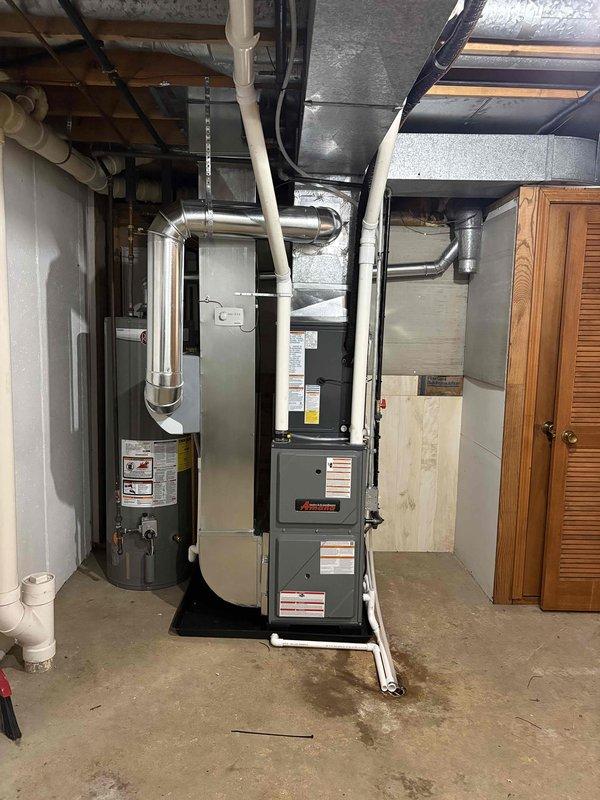 Completed full installation of residential HVAC system including new furnace and air conditioning condenser unit. Installed gray furnace unit in basement mechanical room with proper venting through white PVC piping and connected metallic ductwork with reflective insulation. Positioned outdoor AC condenser unit on concrete pad between buildings with appropriate clearances, ran refrigerant lines using insulated copper tubing, and completed electrical connections. Tested system operation, verified proper airflow through supply and return ductwork, confirmed refrigerant charge levels, and ensured all safety controls functioning correctly. System commissioned and left in full operational status.