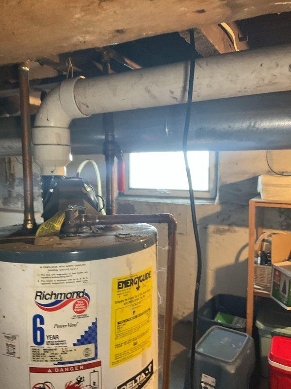 Provided estimate for replacement of existing Richmond 6-year warranty water heater located in basement utility area. Unit is secured with blue metal straps and features standard copper supply piping with brass shut-off valve and white PVC venting system. Documented current installation configuration including piping layout, venting arrangement, and equipment accessibility for replacement proposal.