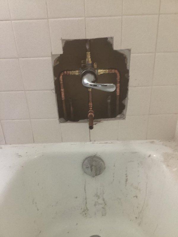 Completed shower valve replacement in tiled bathtub enclosure. Removed existing three-handle chrome valve assembly, cut access opening in tile wall to expose copper supply lines, installed new valve body with updated trim plate, and restored wall opening. System tested and operational upon completion.