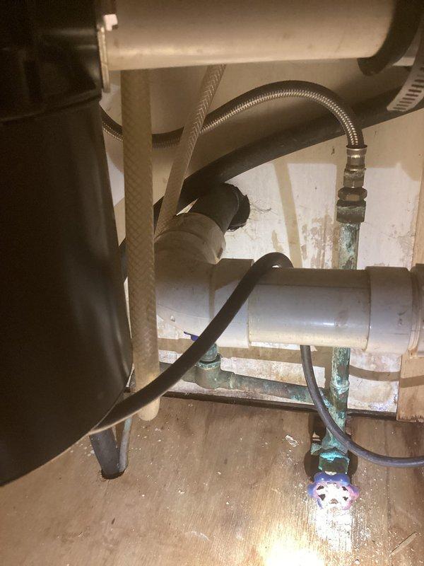 Responded to plumbing leak complaint involving sink drain and suspected wall leak. Upon inspection, identified corroded brass fittings with significant verdigris buildup beneath fixture, along with deteriorated drain connections showing evidence of prolonged water exposure. Documented white mineral deposits and water damage on surrounding wooden cabinetry, confirming active leak conditions. Photographed corroded plumbing assembly including flexible supply lines, PVC drainage components, and compromised metal fittings for service records. Assessed laundry area plumbing infrastructure including overhead utility installations and vertical pipe runs with shut-off valves to determine extent of moisture intrusion.