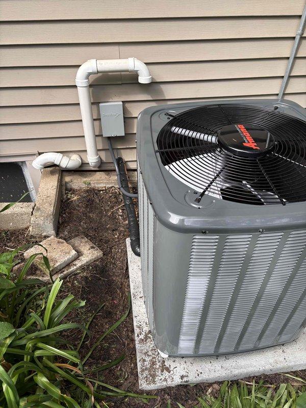 Completed full HVAC system replacement including outdoor condensing unit and indoor air handler. Installed new condenser on existing concrete pad with proper refrigerant line connections and condensate drain piping routed through exterior wall-mounted PVC system. Connected electrical service to outdoor disconnect box and verified proper power supply. Indoor equipment positioned in basement utility area with appropriate venting configuration and all safety labels intact. System tested for proper operation, refrigerant charge verified, and all connections leak-checked and secured.