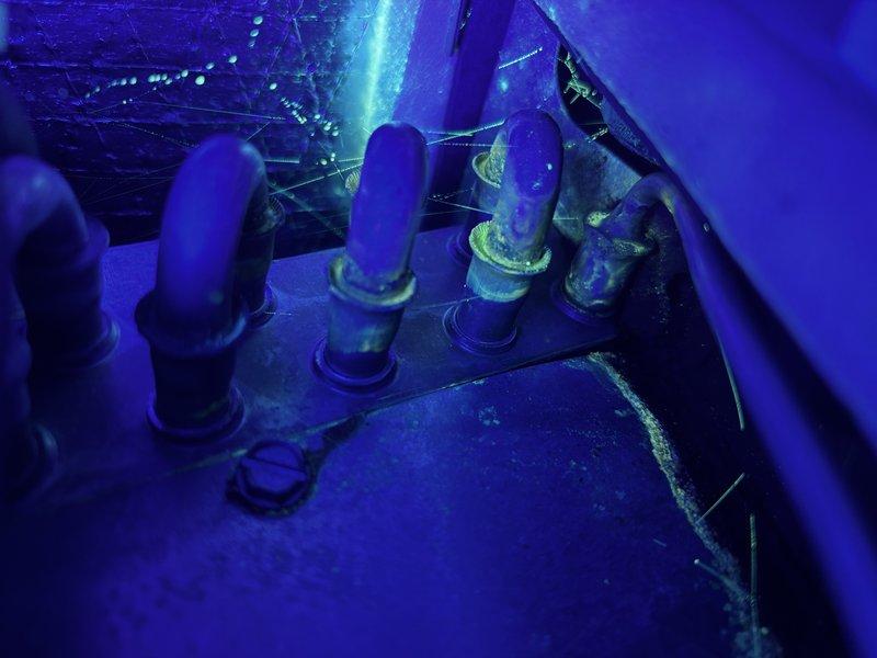 Responded to no-cool condition on 6-year-old unit following previous service visit where UV dye was added to refrigeration system for leak detection. Performed UV light inspection of refrigerant lines and system components, identifying leak location at line set connections. Unit found inoperative due to low refrigerant charge from active leak. Documented findings with UV photography showing fluorescent dye evidence at piping penetrations through base platform.
