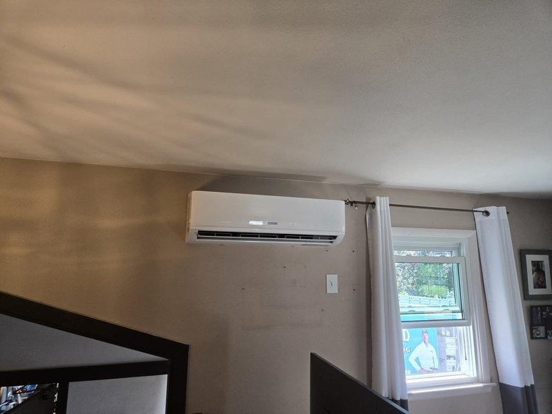 Successfully completed installation of ductless mini-split air conditioning system in residential living space. Mounted indoor evaporator unit on interior wall at optimal height for efficient air distribution, ensuring proper clearance from ceiling and adjacent doorways. Installed unit between window and entertainment area with professional wire management and secure wall mounting. System tested and verified operational, providing climate control capability to the living space.