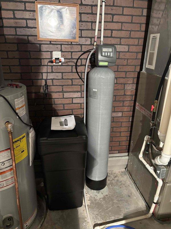 Responded to service call for non-operational water softener system approximately 4 years old. Upon arrival, performed diagnostic assessment of water softening equipment located in basement utility area. Inspected digital control head, brine tank with salt levels, resin tank, and associated plumbing connections including bypass valve and distribution lines. Verified adequate salt pellet supply in brine tank and examined control panel display for error codes or operational indicators. Checked system programming, regeneration cycle settings, and water flow through inlet and outlet connections. Documented existing equipment configuration with water heater and HVAC systems in mechanical room for service records.