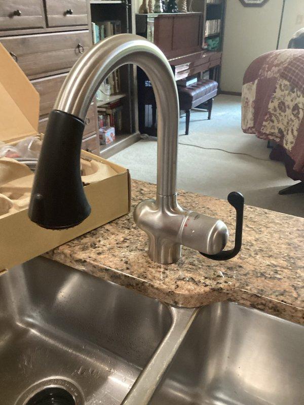 Completed kitchen faucet replacement with customer-supplied fixture on granite countertop with stainless steel double-basin sink. Removed existing faucet assembly, installed new brushed nickel single-handle faucet with pull-down spray head, tested for proper operation and verified no leaks.