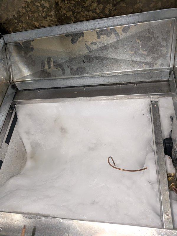Responded to water leak concern at furnace when AC unit was activated. Upon inspection, found water accumulation in condensate drain pan of air handling unit. Examined 3-year-old furnace and 10-month-old Carrier AC system. Inspected drain pan for proper drainage, checked condensate line routing, and verified trap configuration. Documented moisture staining and mineral deposits in collection pan indicating drainage issue. Photographed affected components showing water damage patterns on interior surfaces and discoloration in drain pan assembly. Assessed condensate management system for blockages or improper pitch that would cause water backup into furnace cabinet when cooling system operates.