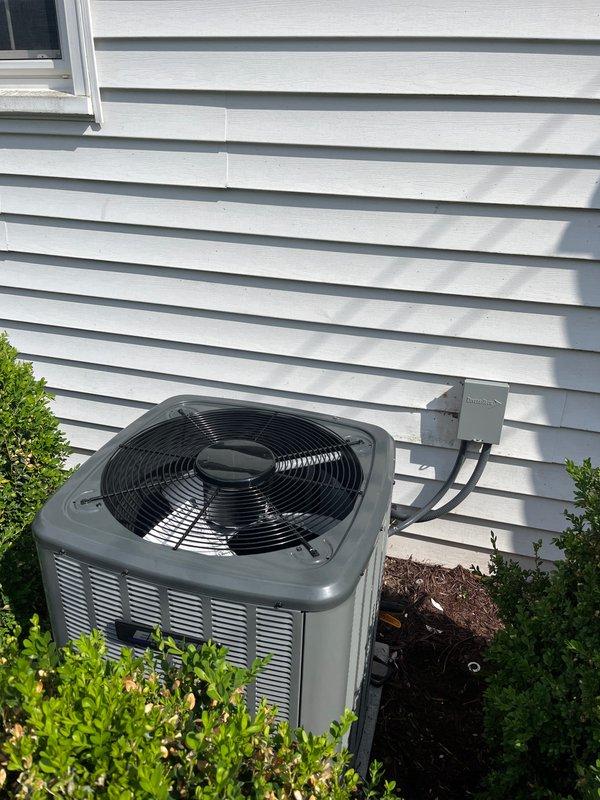 Completed full HVAC system replacement including outdoor condenser unit and indoor air handler. Installed new gray residential condenser with proper clearance from building exterior, connected electrical disconnect box with appropriate conduit routing, and positioned unit on stable pad with adequate drainage. Inside utility space, installed furnace with integrated air handler, configured white PVC venting system extending to exterior, and connected all necessary ductwork including galvanized sheet metal and flexible ducting. Verified proper electrical connections, tested refrigerant lines, confirmed condensate drainage operation, and ensured all safety labels and manufacturer specifications were clearly visible. System commissioned and tested for proper heating and cooling operation with all components functioning within normal parameters.
