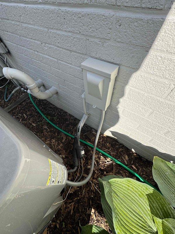 Completed comprehensive AC replacement estimate for residential property. Documented existing outdoor condenser unit mounted on wooden platform with copper refrigerant lines, exterior electrical panel, and associated utility connections. Photographed current system configuration and surrounding area to provide detailed assessment for replacement equipment sizing and installation requirements.