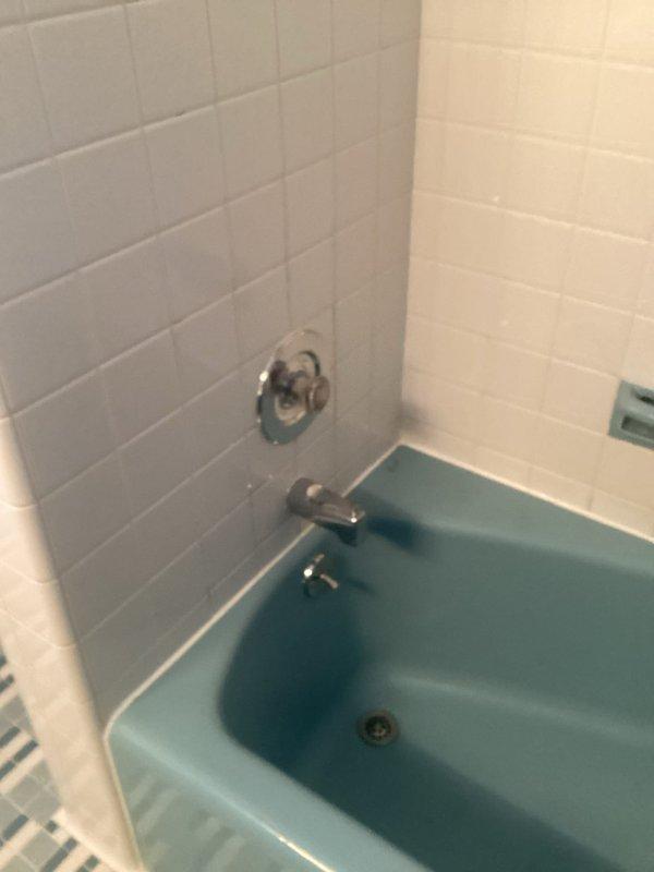 Responded to HVAC-identified water leak originating from bathtub and infiltrating basement area. Inspected vintage turquoise bathtub installation with chrome fixtures, including combination faucet, shower control, and diverter valve assembly. Documented existing conditions of tub surround with white subway tile walls and plumbing connections to assess source of water intrusion and provide recommendations for repair.