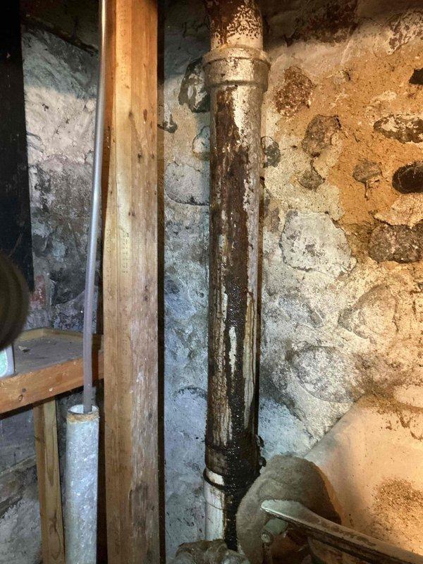 Responded to plumbing leak occurring during washing machine operation. Upon inspection, discovered severely corroded vertical drain pipe in basement with active water infiltration causing significant moisture damage to surrounding wooden framing and foundation walls. Documented extensive rust deterioration on metal piping and water staining patterns on structural elements. Identified compromised drainage system as source of leak activated by washing machine discharge cycles.