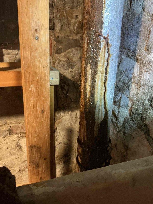 Responded to plumbing leak occurring during washing machine operation. Upon inspection, discovered severely corroded vertical drain pipe in basement with active water infiltration causing significant moisture damage to surrounding wooden framing and foundation walls. Documented extensive rust deterioration on metal piping and water staining patterns on structural elements. Identified compromised drainage system as source of leak activated by washing machine discharge cycles.