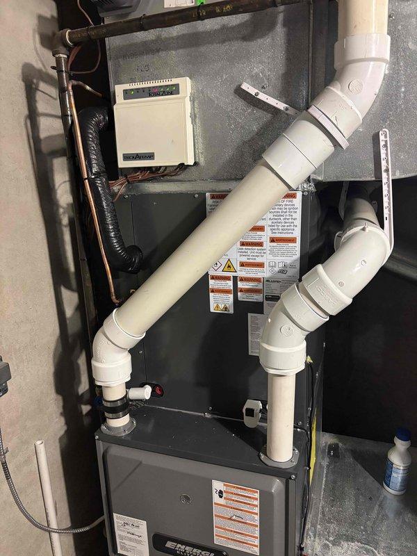 Completed full HVAC system replacement including indoor furnace unit and outdoor condenser. Installed new furnace in utility closet with proper venting using white PVC intake and exhaust pipes, connected refrigerant lines with insulation, and mounted wall control. Positioned new outdoor condenser unit against stone wall with proper clearance, ran electrical conduit, and verified system startup and operational parameters within manufacturer specifications.