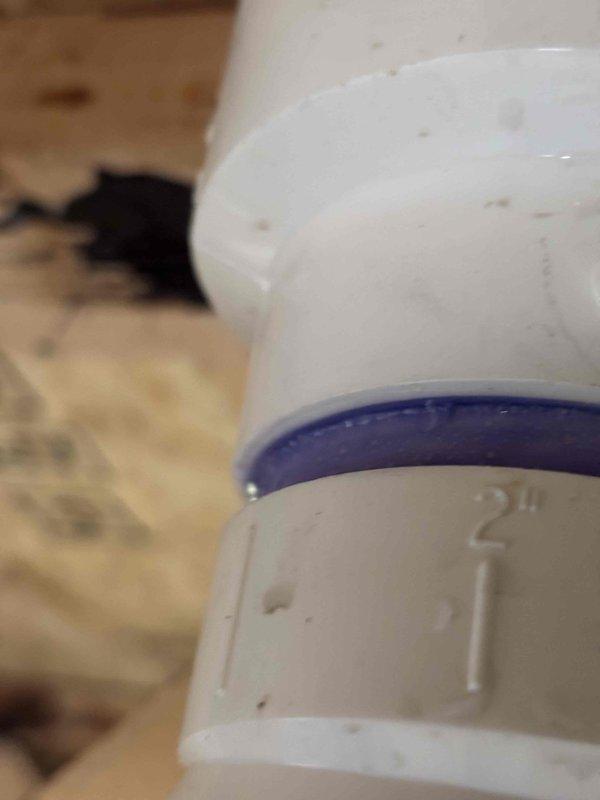 Responded to water leak complaint originating from HVAC distribution box in attic space. Inspected 18-year-old system and located active dripping from condensate drain line assembly. Found PVC drain piping with compromised seal at coupling joint, evidenced by moisture staining on adjacent wooden framing members. Documented pipe configuration and leak source with photographic evidence. System confirmed operational for both heating and cooling functions at time of inspection. Advised potential connection to previous water damage incident from April.
