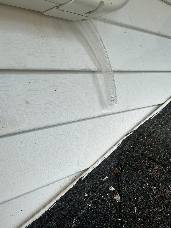 Responded to water leak complaint regarding minisplit head unit in living room draining down interior wall and causing flooding at exterior mailbox location. Upon inspection, identified improper condensate drainage from the indoor air handler unit. Traced condensate line routing from interior unit to exterior discharge point and discovered drainage issue at building envelope penetration where line exits structure. Documented exterior wall and roof junction area showing condensate discharge location and evidence of water intrusion pathway. Recommended proper condensate line installation with appropriate pitch, secure mounting, and verified termination point away from building foundation and mailbox area to prevent future water damage.