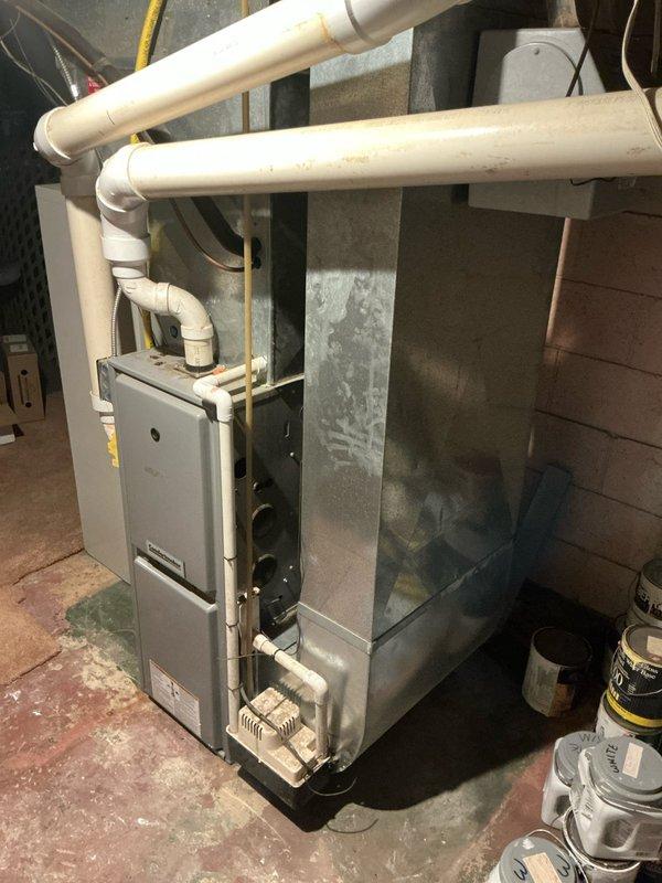Completed estimate for aging but operational furnace and air conditioning system. Inspected basement-installed gray metal furnace with exposed internal components and high-efficiency white PVC intake/exhaust venting showing dust accumulation, and evaluated outdoor condenser unit with protective wire cage, heavily soiled top cover, wall-mounted disconnect and controls, situated on concrete pad with landscaping. Provided replacement recommendations for both heating and cooling equipment based on age and condition assessment.