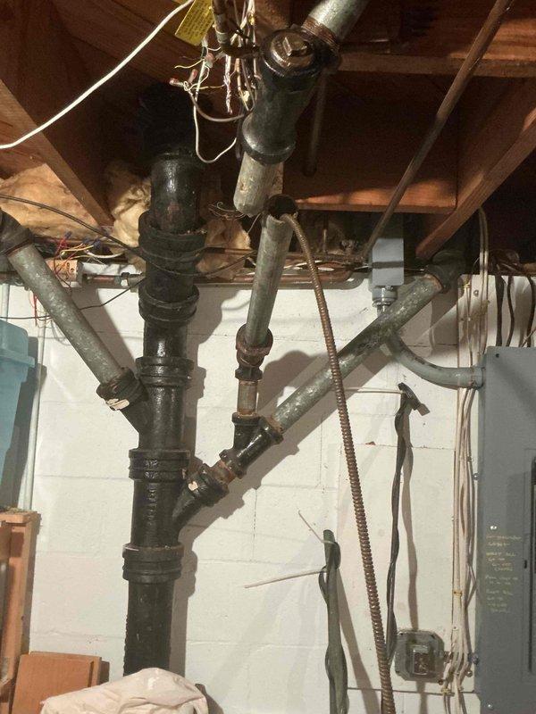 Responded to multiple plumbing issues in a 75-year-old residential property including clogged drain, leaky kitchen faucet, leaky bathroom faucet, and shower malfunction that had persisted for several weeks. Inspected basement plumbing infrastructure including aged cast iron drain stack system with multiple branch connections and vertical piping assembly. Cleared drain obstruction using cable auger equipment, repaired both faucet leaks by replacing worn washers and valve components, and addressed shower fixture issue. Documented existing plumbing conditions including vintage cast iron drain system with metal clamps and fittings, exposed joists in basement utility area, and wall-mounted conduit installations. All reported plumbing problems resolved and systems restored to proper working order.