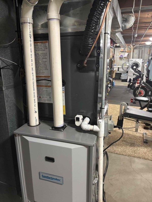 Completed full air conditioning system replacement in residential basement utility area. Removed existing AC unit and installed new ComfortMaker HVAC system with proper venting configuration using white PVC piping extending vertically from unit through ceiling joists. Connected black flexible ductwork to system for air distribution. Ensured all refrigerant lines, condensate drainage, and electrical connections were properly installed and secured. Verified system operation, airflow, and temperature output. Unit positioned on concrete floor against cinderblock wall with adequate clearance for service access. All installation work performed to manufacturer specifications and local code requirements. System tested and operational upon completion.