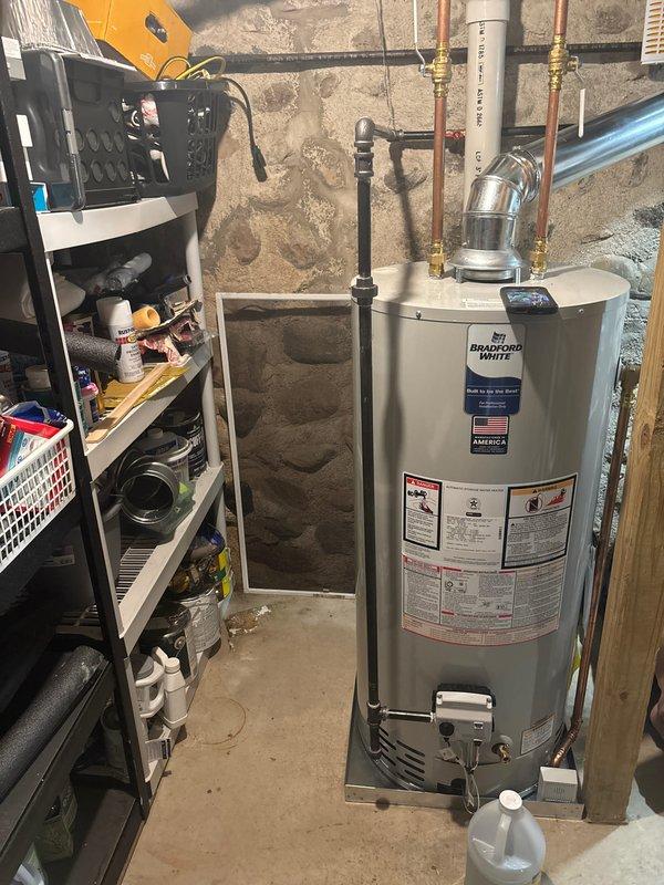 Completed full installation of residential HVAC system including furnace, air conditioning unit, and water heater. Installed Bradford White water heater in basement utility area with copper piping and brass fittings connected to existing plumbing infrastructure along stone foundation wall. Mounted outdoor AC condenser unit on concrete pad in side yard with proper electrical connections, refrigerant lines, and black corrugated conduit running to interior equipment. All units tested and verified operational upon completion of installation.