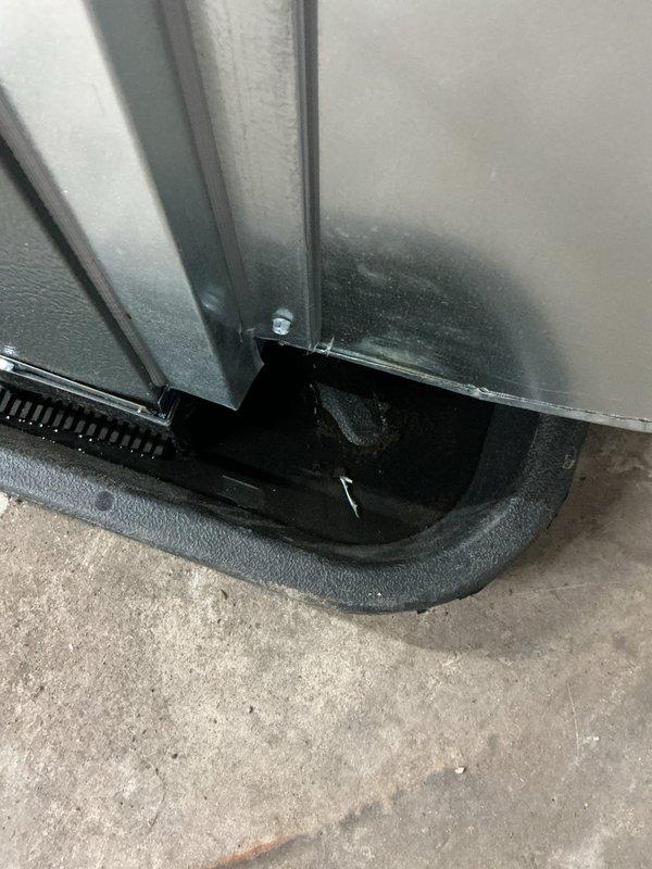 Responded to service call for air conditioning system with reported cracked condensate pan leaking water into furnace and pinched refrigerant line. Upon arrival, performed thorough inspection of outdoor condenser unit and indoor components. Found condenser unit with severely clogged protective cage, fins, and mesh filter heavily restricted with accumulated dirt, dust, and debris buildup indicating extended period without maintenance. Documented condition of drainage system at base of unit including black plastic drain pan component and concrete pad installation. Photographed extent of debris accumulation on cylindrical condenser unit which was completely obscuring internal components and significantly impacting airflow and system efficiency. Assessed reported concerns regarding condensate pan integrity and refrigerant line condition for further evaluation and repair recommendations.