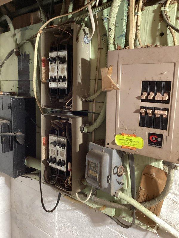 Conducted comprehensive estimate for air conditioning system installation and electrical panel upgrade. Evaluated existing electrical infrastructure, which included outdated electrical panels with exposed circuit breakers, aging wiring configurations, and current meter installation on exterior wall. Assessed electrical capacity requirements for new AC system integration, determining that panel upgrade would be necessary to support additional load demands. Documented existing conditions including legacy electrical boxes with visible wear, seafoam-colored conduit network, and newer beige panel with circuit breaker arrangement. Photographed exterior meter assembly with PVC conduit system and interior utility space showing multiple panel configuration on concrete block wall. Provided detailed recommendations for panel modernization to accommodate air conditioning equipment installation while ensuring compliance with current electrical codes and safety standards.