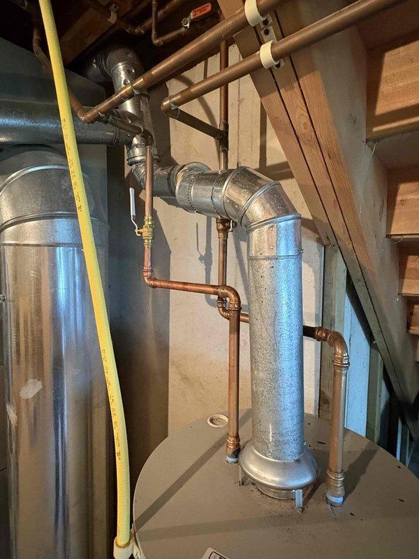 Responded to service call for air conditioning unit providing insufficient cooling. Upon arrival, performed system diagnostic on approximately 10-year-old AC unit. Inspection revealed water heater in mechanical room showing significant rust staining at base and moisture accumulation on exterior surface, indicating potential leak or condensation issue affecting overall HVAC system performance. Documented equipment conditions with photographs showing interconnected plumbing and HVAC infrastructure in basement utility area. Assessed copper refrigerant lines, ductwork connections, and mechanical room environment. Pet dander accumulation noted during inspection, which may contribute to reduced airflow and system efficiency if filters and coils are not maintained regularly. Provided customer with findings and recommendations for addressing cooling deficiency and water heater concerns to restore proper system operation.