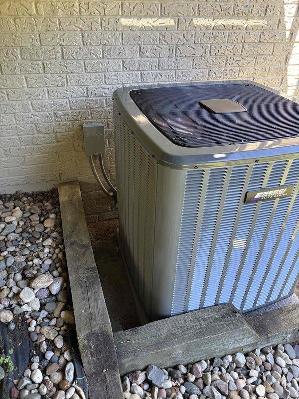 Completed full air conditioning system replacement including indoor air handler unit and outdoor condenser unit. Indoor installation included vertical air handler with integrated humidifier system, Trane AirBear filtration system, proper electrical connections, and secure mounting within metal frame structure in basement utility area. Outdoor condenser unit installed on elevated wooden platform with decorative stone landscaping, properly leveled and secured against exterior foundation wall with appropriate electrical disconnect and conduit routing. All components tested and verified operational upon completion.