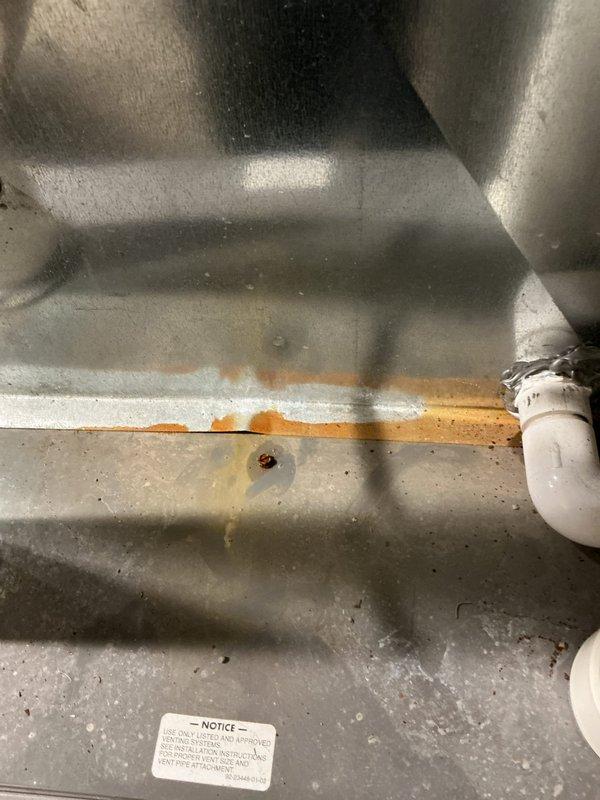 Responded to water leak complaint beneath furnace with unusual noises. Upon inspection, discovered active water accumulation on utility room floor originating from HVAC condensate drainage system. Identified rust staining and corrosion along drain pan seam on 11-year-old furnace unit, indicating compromised pan integrity. Documented water pooling with visible foam accumulation and mineral deposits in drain pan, confirming condensate drainage issue rather than furnace malfunction. PVC drainage piping appeared intact with no visible damage. System currently maintaining heating and cooling functionality despite drainage concern. Photographed affected areas including floor water accumulation and corroded drain pan for documentation purposes.