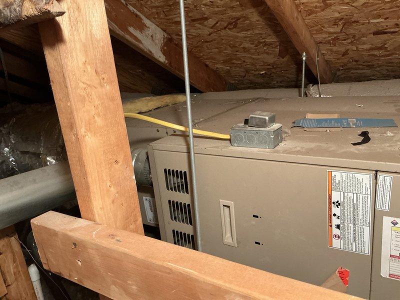 Conducted furnace replacement estimate for residential property with 22-year-old existing heating system located in attic space. Inspected current HVAC equipment installation, documented unit condition and configuration, photographed existing furnace with visible manufacturer specifications and warning labels, assessed attic accessibility and structural clearances for potential replacement unit, and evaluated electrical connections and ductwork routing. Exterior air conditioning condenser unit also documented during site assessment.