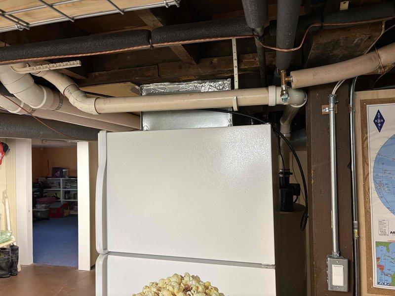 Conducted comprehensive assessment of existing water heater system and associated plumbing infrastructure in basement utility area. Documented current mechanical installation including pump assembly, copper and PVC piping configurations, and existing equipment conditions showing age-related wear and patina on copper lines. Photographed overhead plumbing systems, exposed joists, ductwork, and utility room layout to provide detailed estimate for water heater replacement.