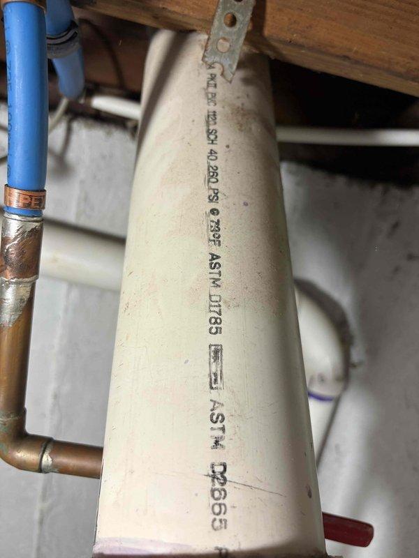 Conducted comprehensive site assessment for water heater replacement, documenting existing plumbing infrastructure in crawl space and exterior drainage configuration. Photographed current PVC and copper supply line connections beneath floor joists, noting condition of pipe supports and existing fittings, as well as exterior discharge piping and foundation clearances to determine proper installation requirements and material specifications for new water heater system.