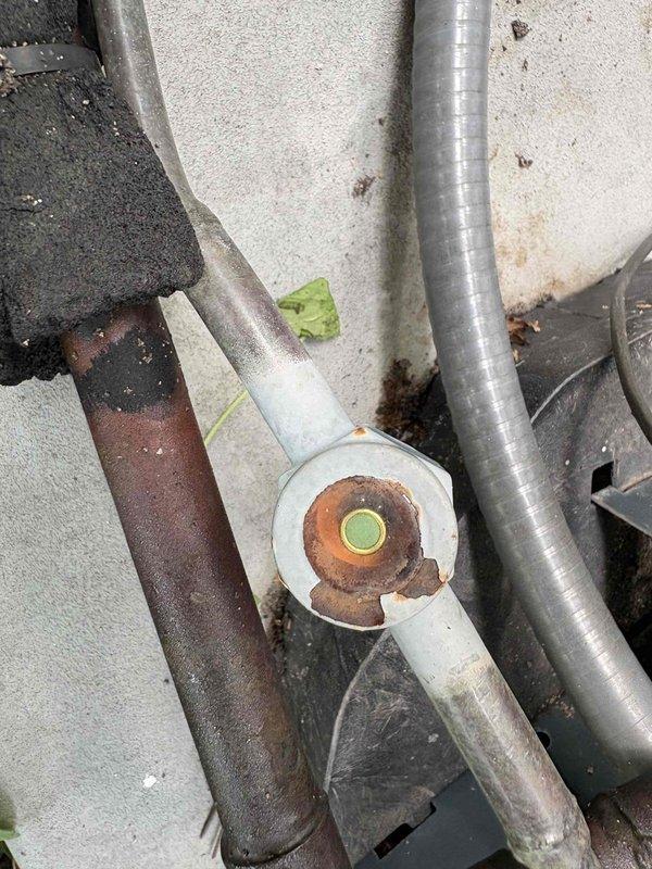 Responded to no cooling complaint on residential air conditioning system. Upon arrival, performed visual inspection of indoor air handler and outdoor condensing unit. Documented significant rust and corrosion present on refrigerant line connections at outdoor unit, indicating prolonged exposure to weather and moisture. Flange connection showed heavy oxidation with visible deterioration that could compromise system integrity. Indoor air handler inspection revealed unit in utility area with proper condensate drain lines installed. Photographed corroded components and equipment labels for documentation purposes. System age could not be determined from available information. Recommended further diagnostic evaluation to assess refrigerant line integrity, check for potential leaks at corroded connections, and determine full extent of repairs needed to restore cooling capacity.