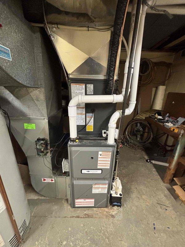 Completed full air conditioning system replacement at residential property. Removed existing AC condensing unit and installed new outdoor condensing unit on concrete pad with proper clearance between structures. Refrigerant lines were installed and insulated, routed along exterior wall through vinyl siding penetration. Indoor air handler was installed in basement utility area with proper integration to existing furnace system. White PVC condensate drainage and venting piping was installed per manufacturer specifications. All electrical connections completed, system charged with refrigerant, and unit tested for proper operation. System startup confirmed satisfactory airflow, temperature differential, and overall performance within manufacturer parameters.