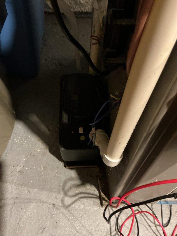 Responded to water leak reported on top of furnace with AC system still operational. Upon inspection, identified moisture accumulation in utility area near HVAC equipment and condensate management components. Examined condensate pump assembly, drainage lines, and associated PVC piping for proper function and potential leak sources. Verified electrical connections and pump operation. Assessed white PVC drain line routing and condensate discharge system. Documented existing conditions including floor moisture patterns and equipment configuration for a 4-year-old system. Photographed affected area showing utility room infrastructure, drainage components, and water-damaged concrete flooring to record leak location and equipment layout.